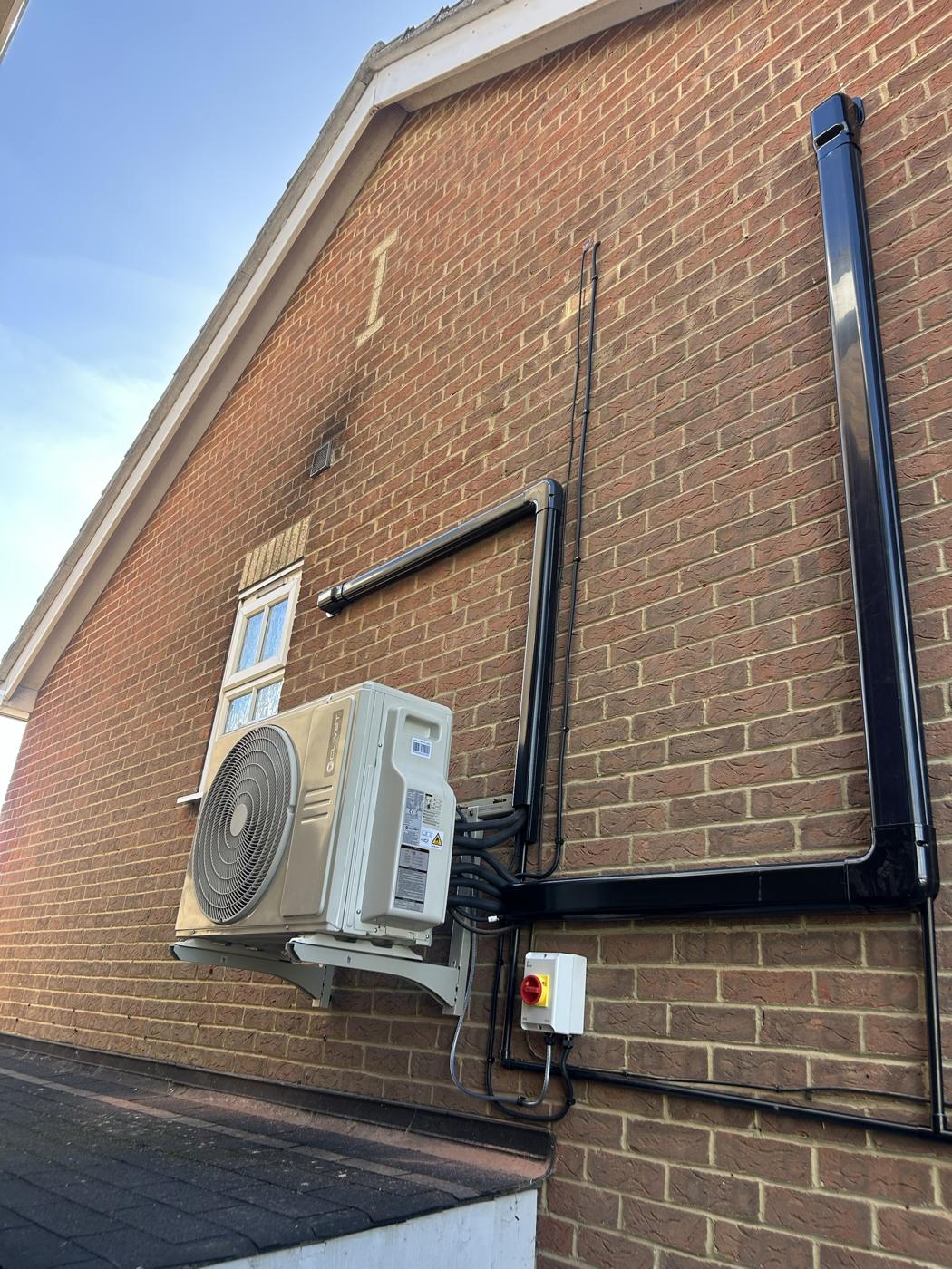 Outdoor air conditioning unit on wall brackets with black trunking running neatly up a brick wall